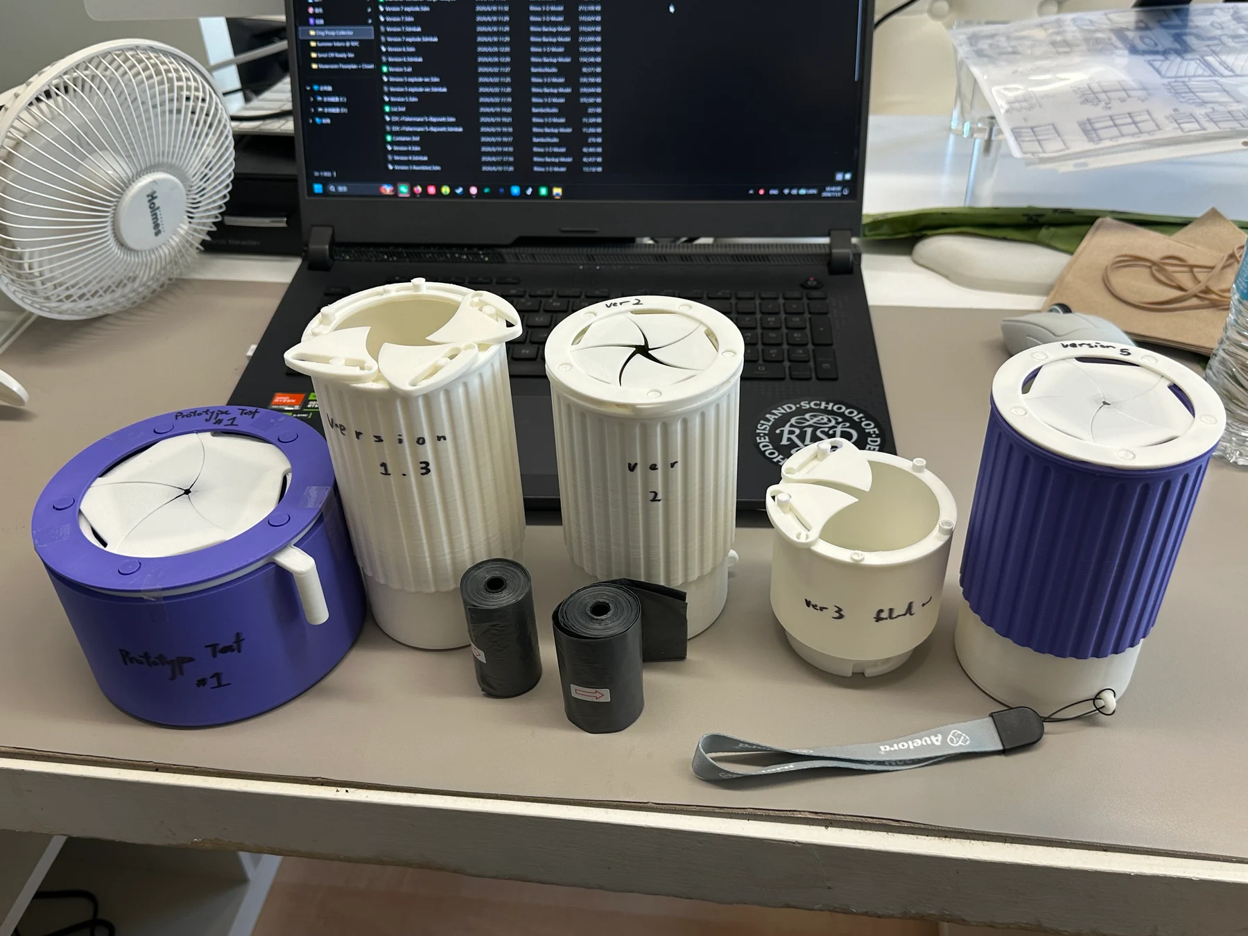 Five physical Iris prototypes on a workbench. The earliest purple prototype at left has a separate white operating lever, identified by the annotation.